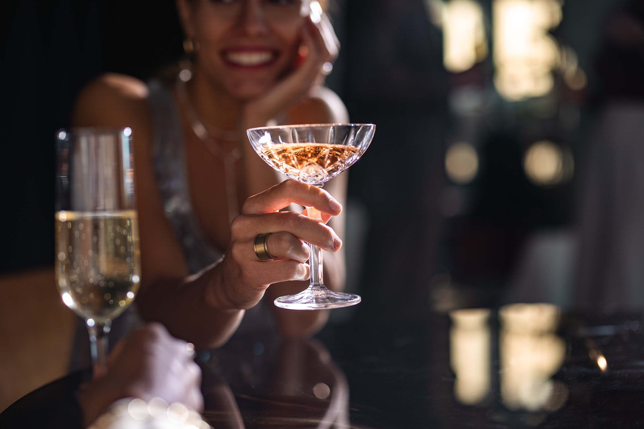 A woman holding a cocktail clinking glasses with a champagne flute