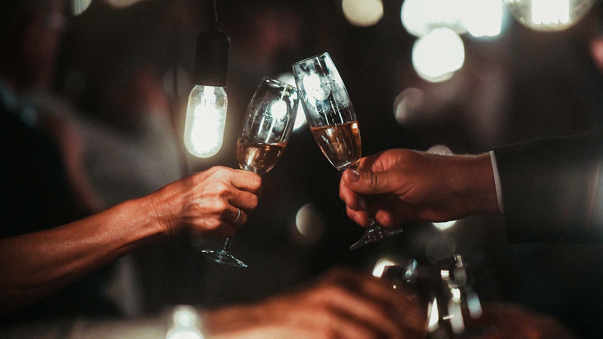 Champagne flute toast with hanging bulbs in a dark room