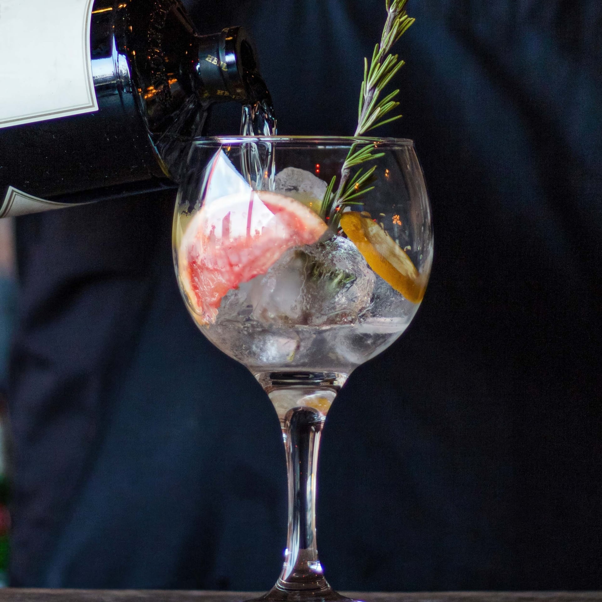 Bartender pouring into a glass with ice, rosemary, and citrus fruits