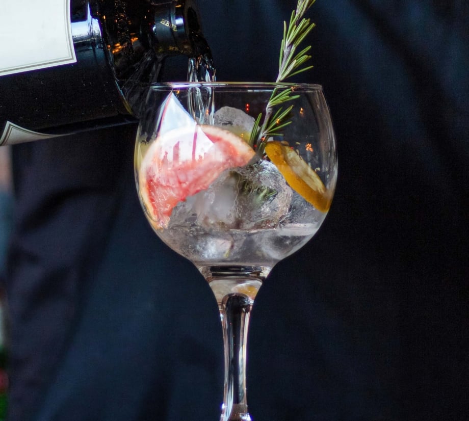 Bartender pouring into a glass with ice, rosemary, and citrus fruits
