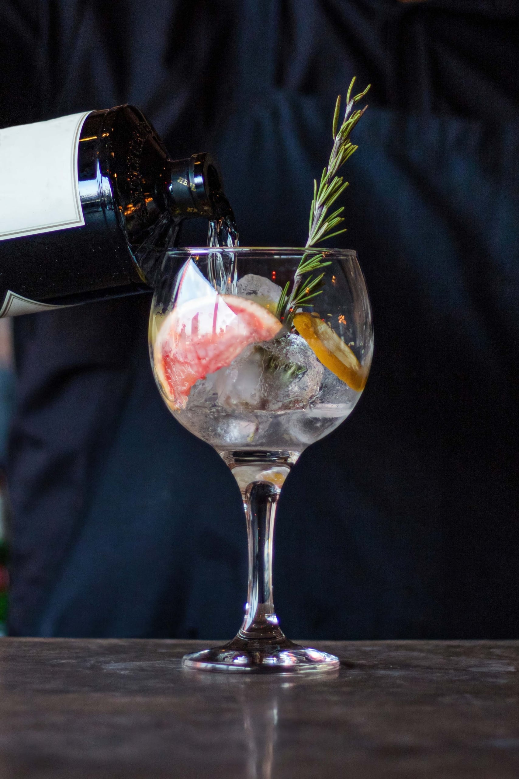 Bartender pouring into a glass with ice, rosemary, and citrus fruits