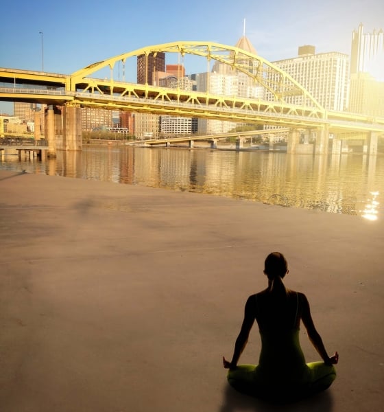 A woman meditating on a beach with a city view