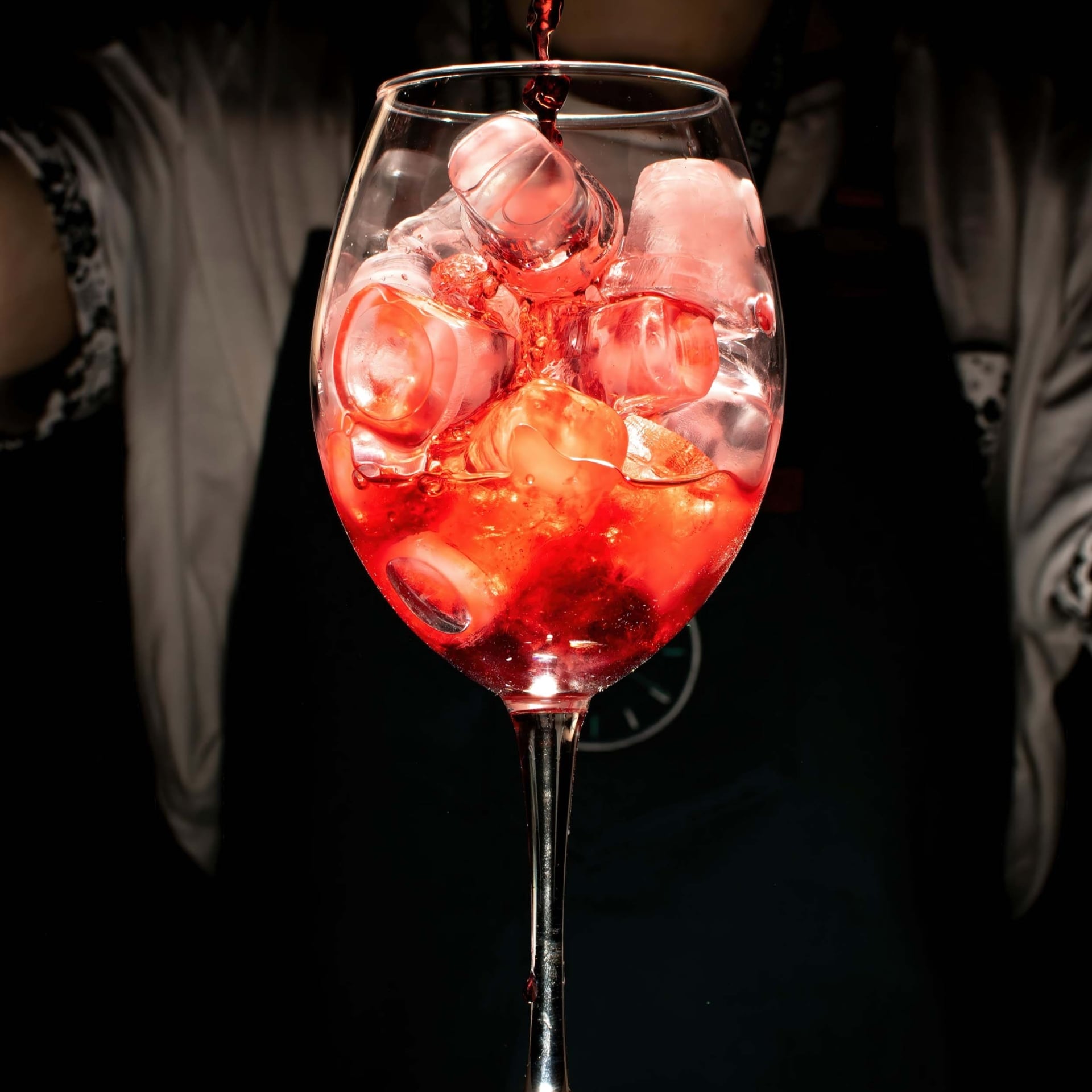 A bartender pours a bright red drink into a glass with ice