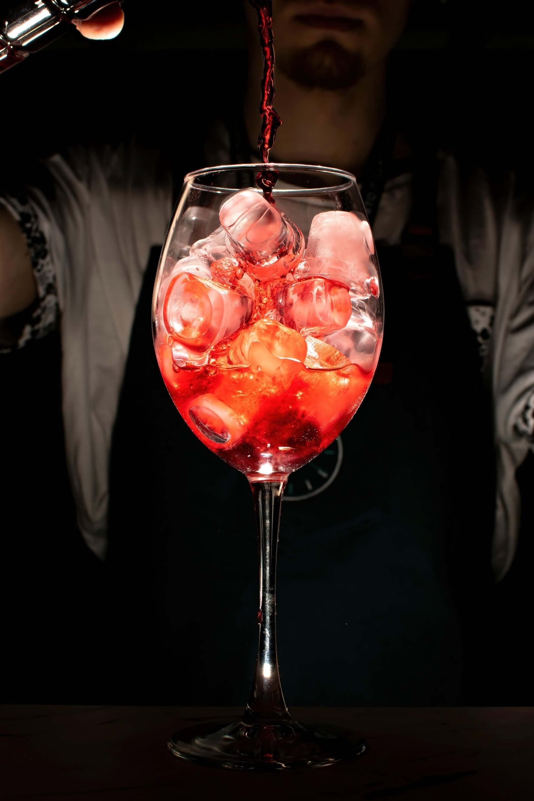 A bartender pours a bright red drink into a glass with ice