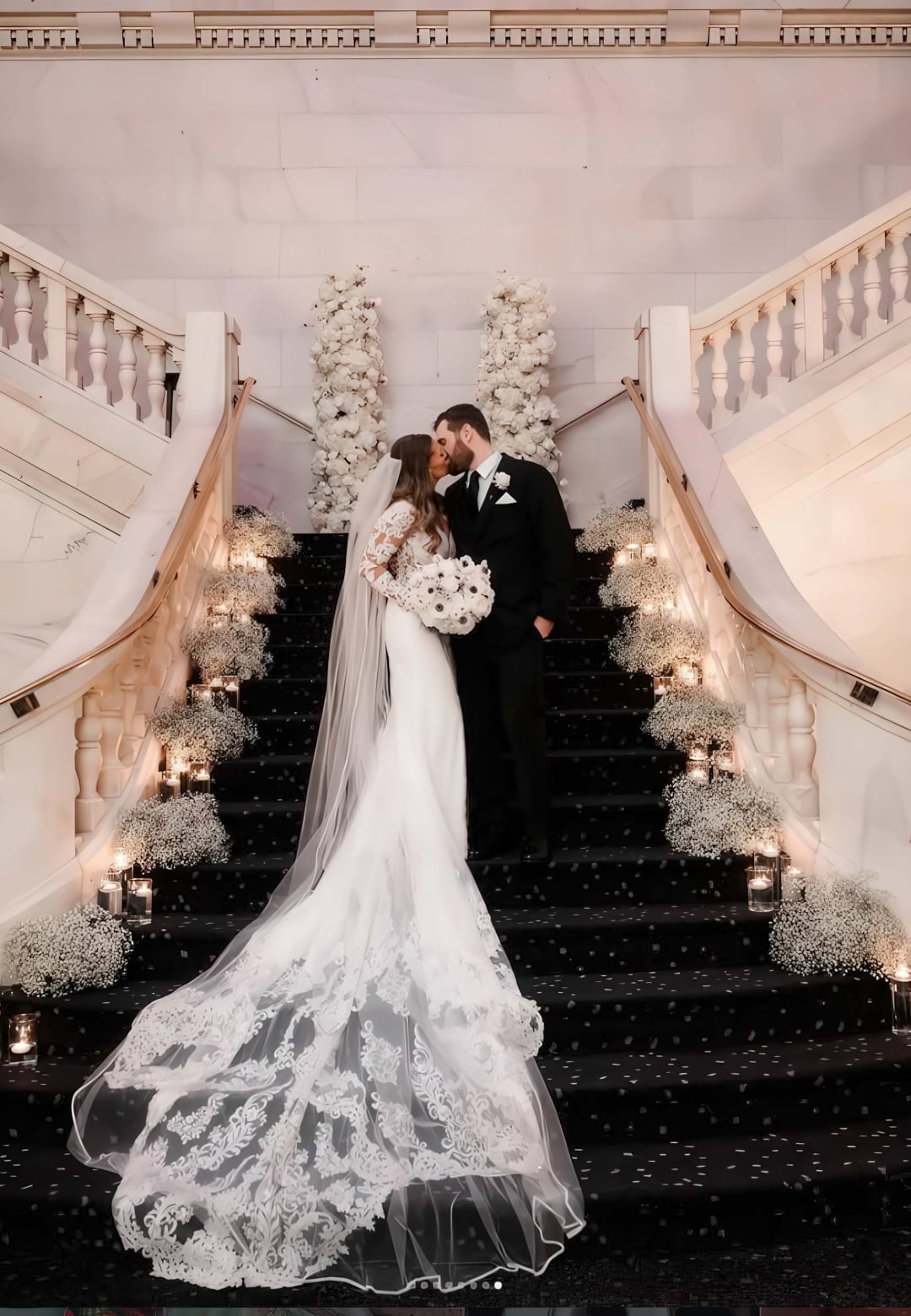 A bride and groom kiss standing on a decorated staircase