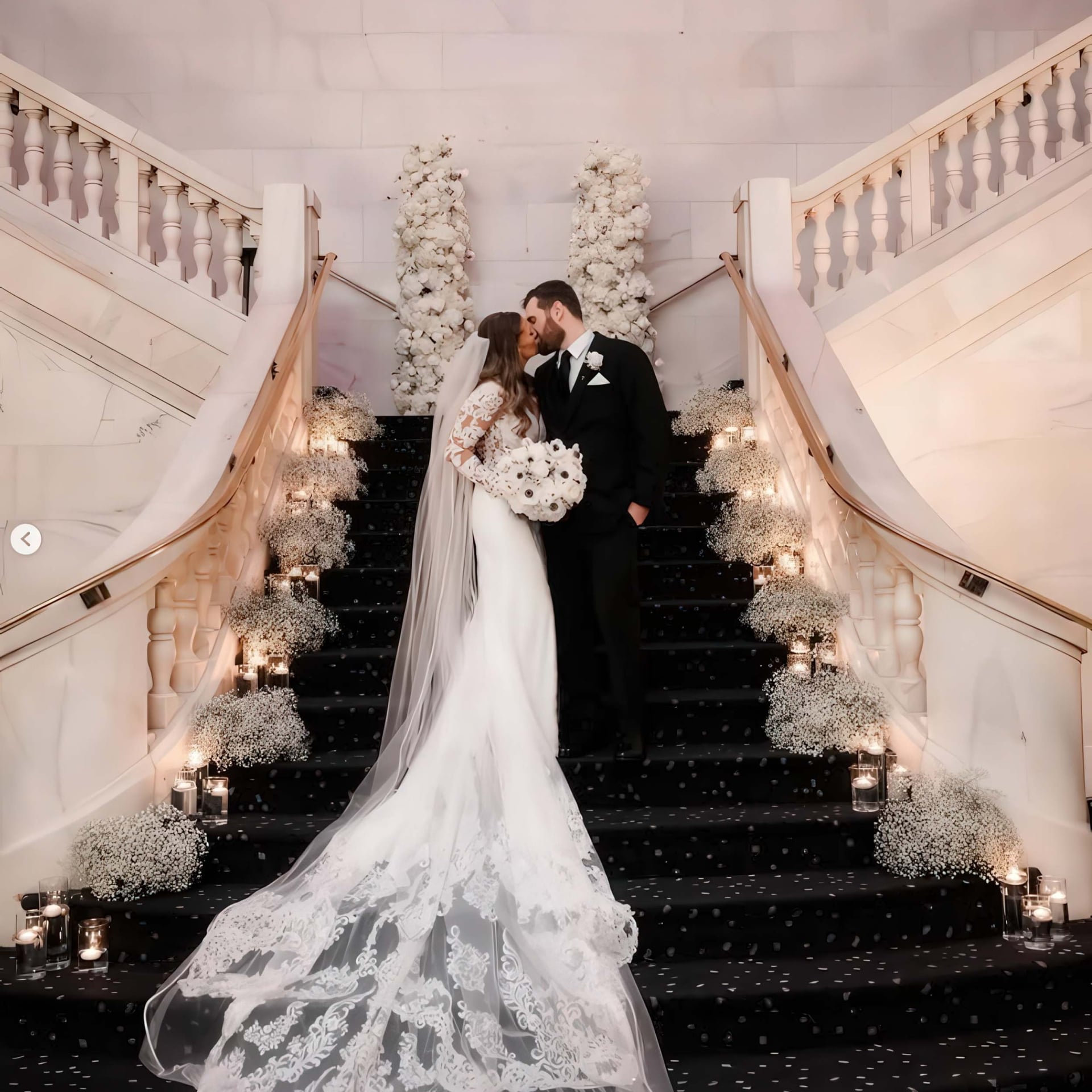 A bride and groom kiss standing on a decorated staircase