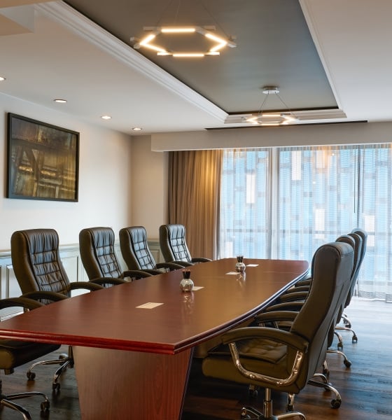Professional boardroom featuring a long wooden conference table, black leather chairs, and modern lighting.