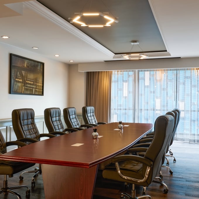 Professional boardroom featuring a long wooden conference table, black leather chairs, and modern lighting.
