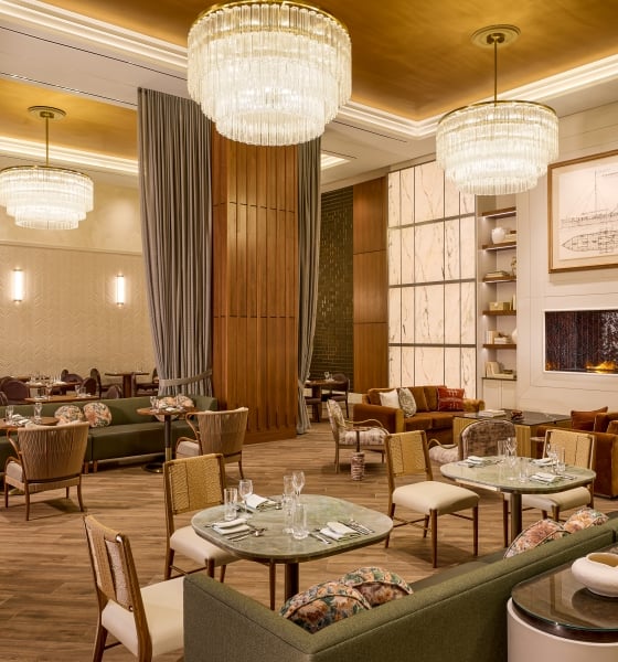 Upscale hotel dining room with marble tables, velvet chairs, wood paneling, and large ring chandeliers.