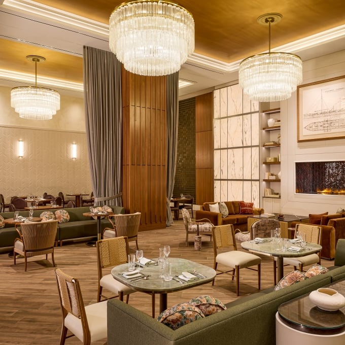 Upscale hotel dining room with marble tables, velvet chairs, wood paneling, and large ring chandeliers.