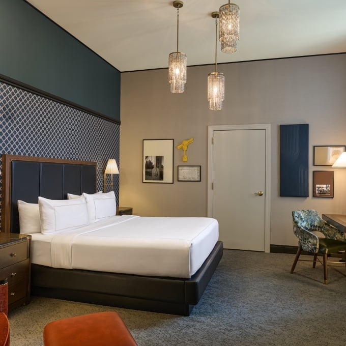 Luxury hotel bedroom with a king bed, patterned wallpaper, three hanging pendant lights, and a desk setup.