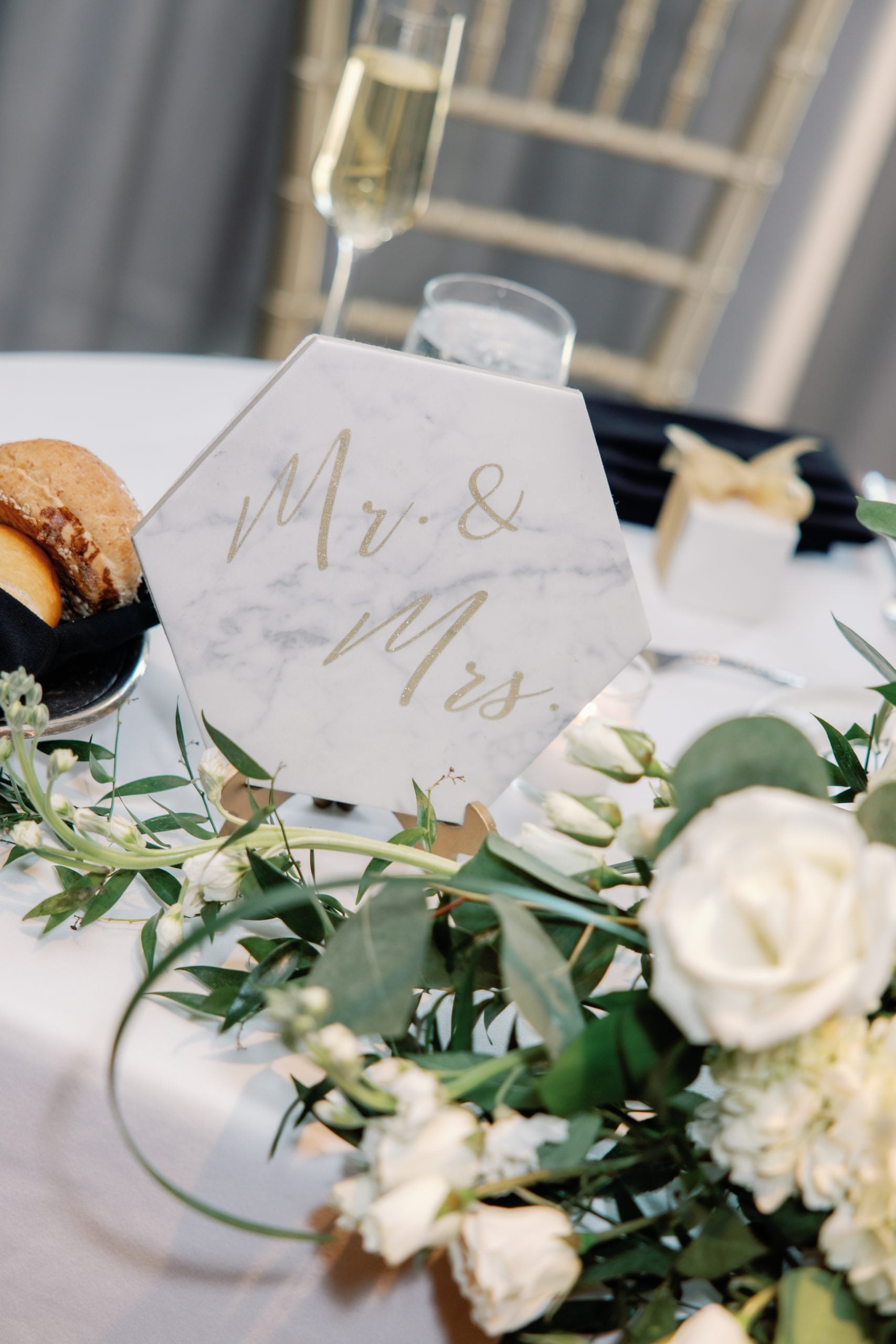 Marble wedding sign reading 'Mr. & Mrs.' on a decorated reception table with a champagne flute and flowers in the foreground