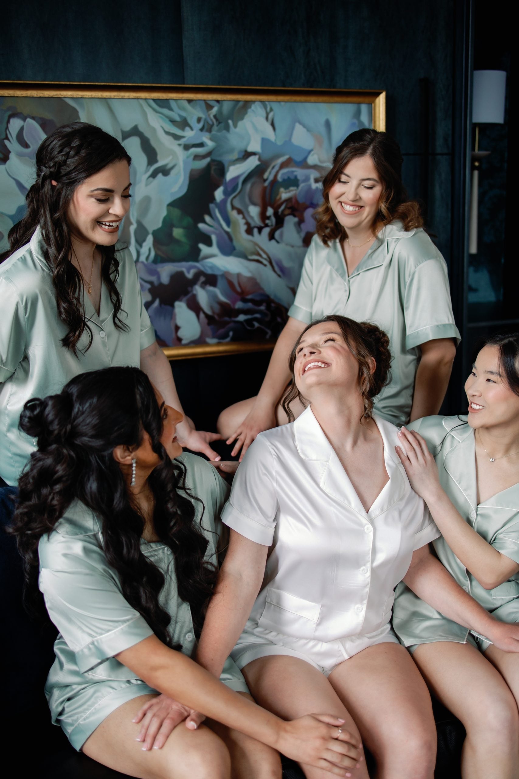 Bridal party wearing satin robes, the bride in white, sharing a joyful moment indoors.