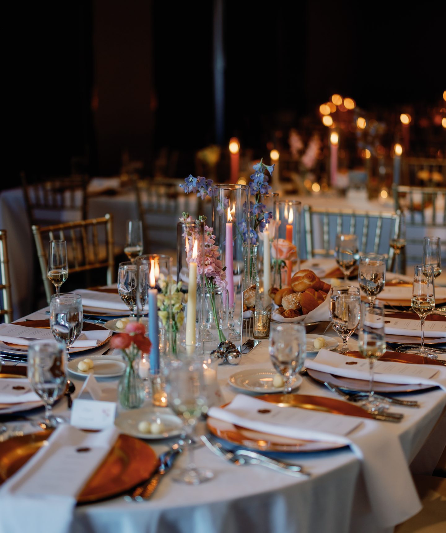 Elegant banquet table set for a formal event with candles, glassware, and floral centerpieces in a dimly lit venue.