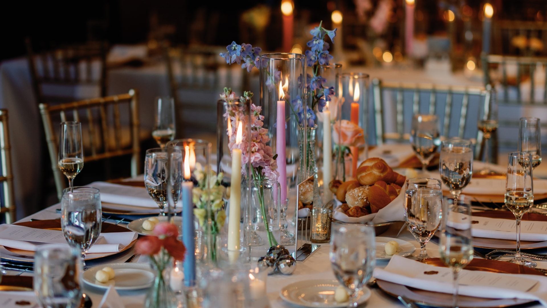 Elegant banquet table set for a formal event with candles, glassware, and floral centerpieces in a dimly lit venue.