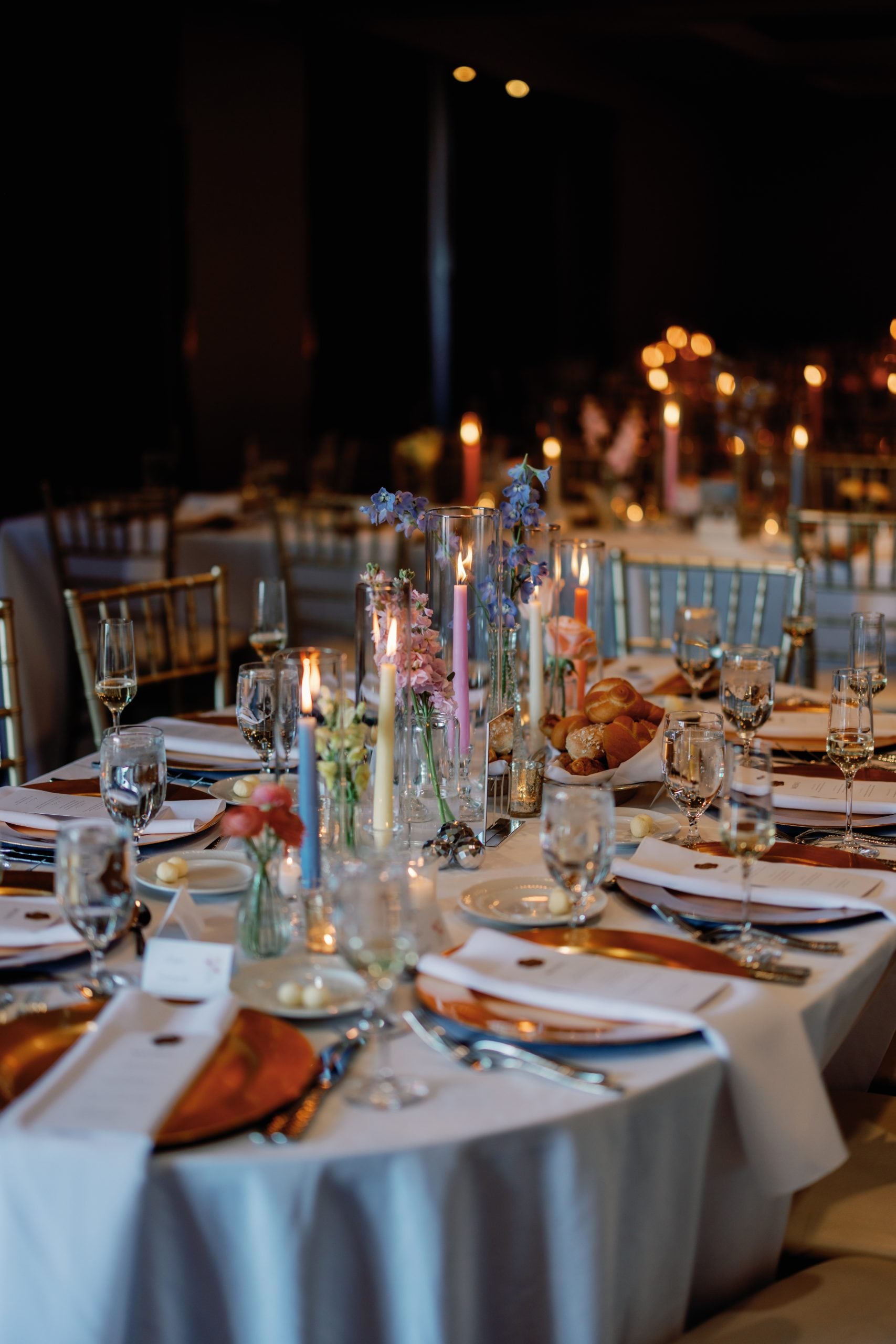 Elegant banquet table set for a formal event with candles, glassware, and floral centerpieces in a dimly lit venue.