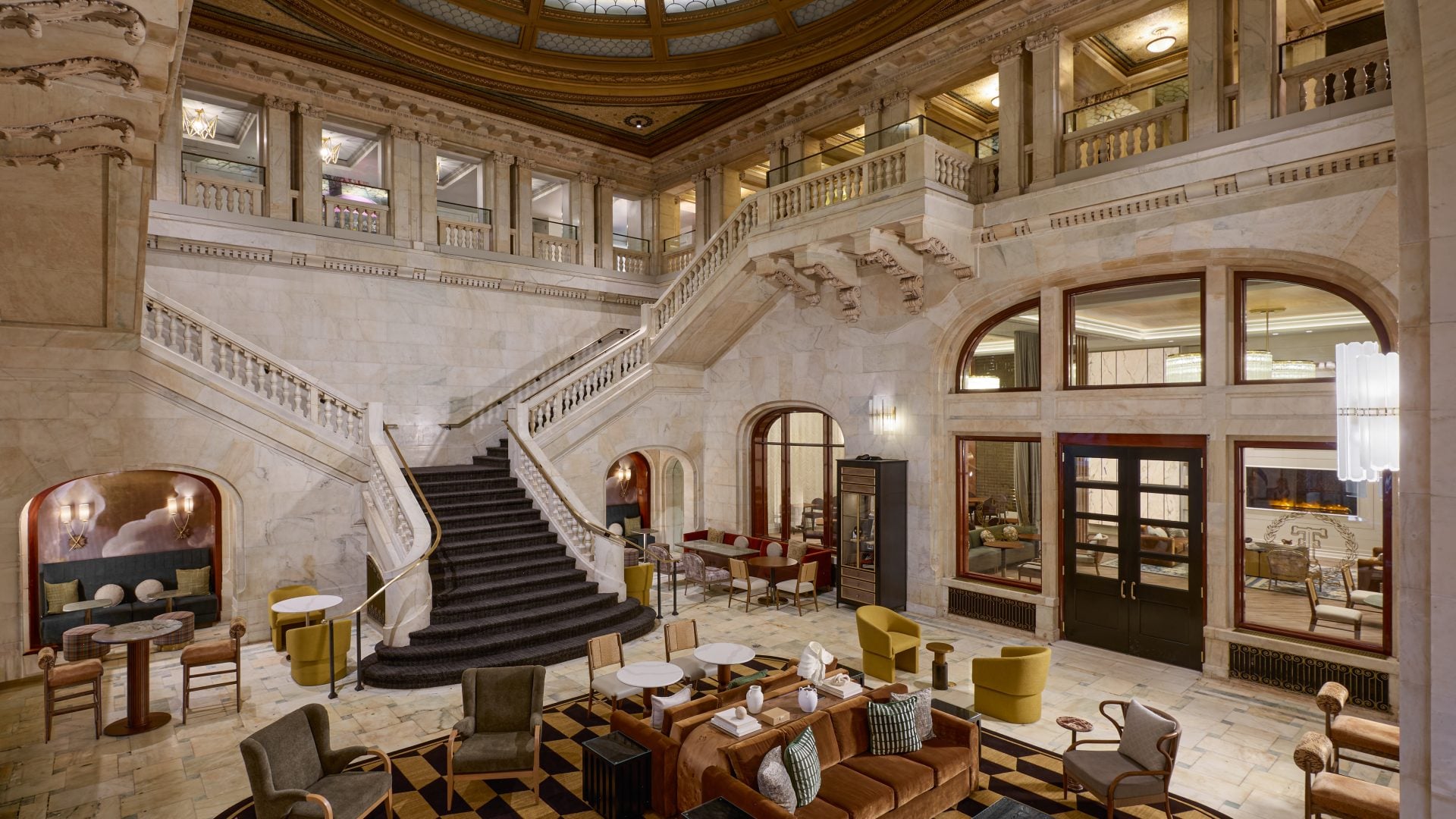 Grand marble hotel lobby with a sweeping staircase, balconies, and a domed glass ceiling.