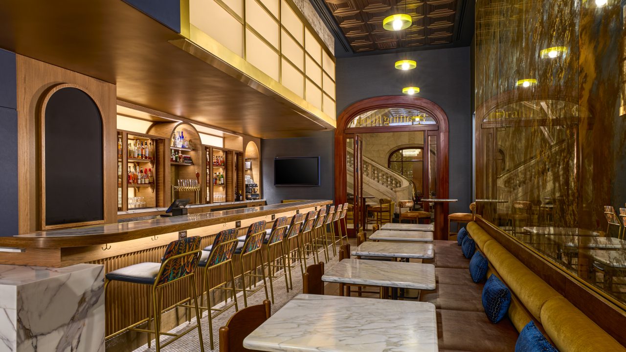 Elegant bar interior with a long marble counter, gold bar stools, and liquor shelves behind the bar under warm pendant lights.