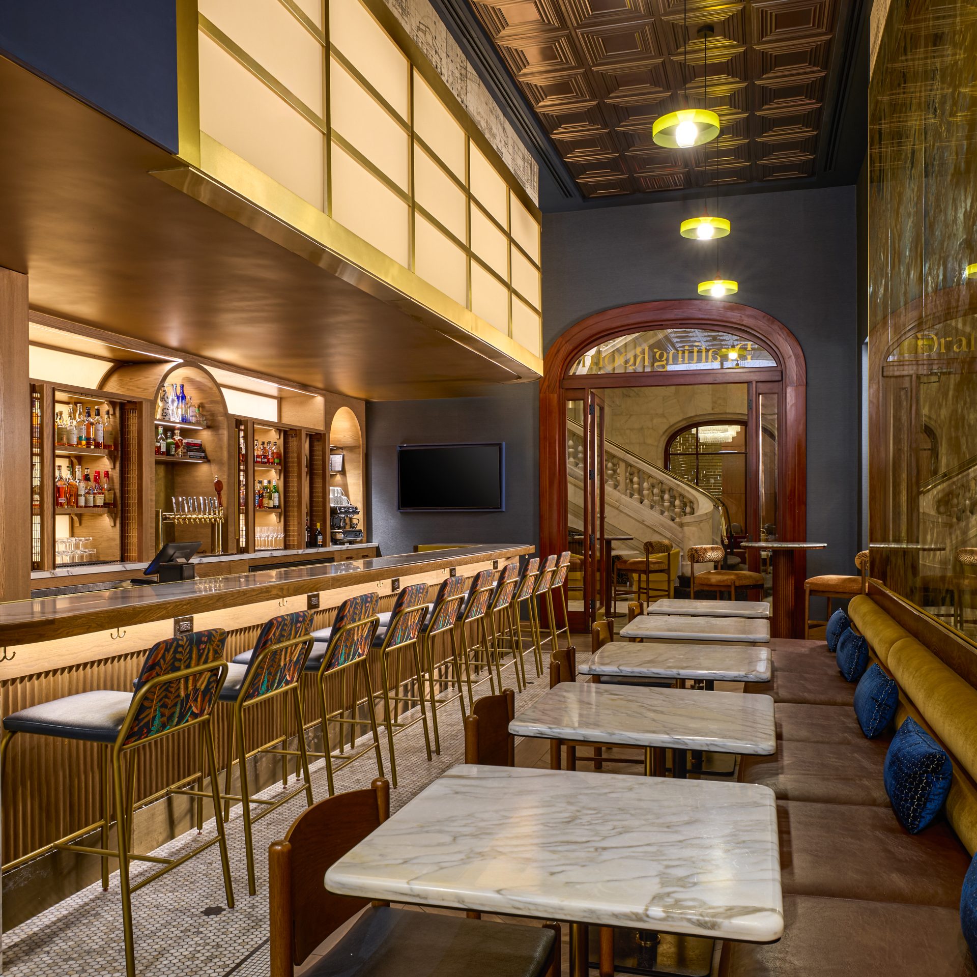 Elegant bar interior with a long marble counter, gold bar stools, and liquor shelves behind the bar under warm pendant lights.