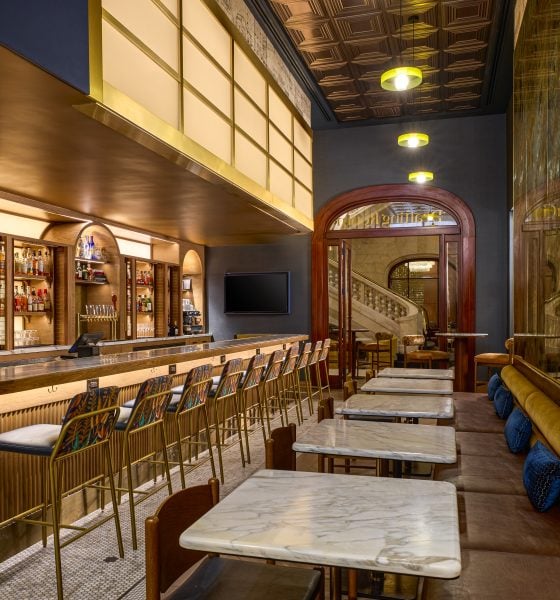 Elegant bar interior with a long marble counter, gold bar stools, and liquor shelves behind the bar under warm pendant lights.