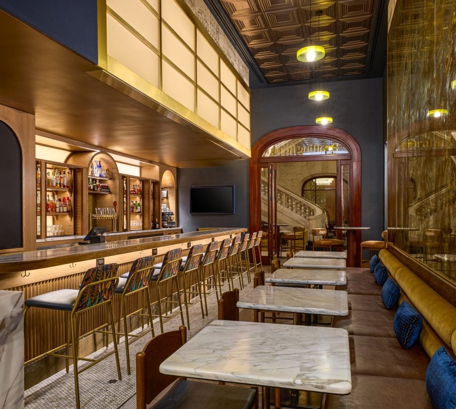 Elegant bar interior with a long marble counter, gold bar stools, and liquor shelves behind the bar under warm pendant lights.