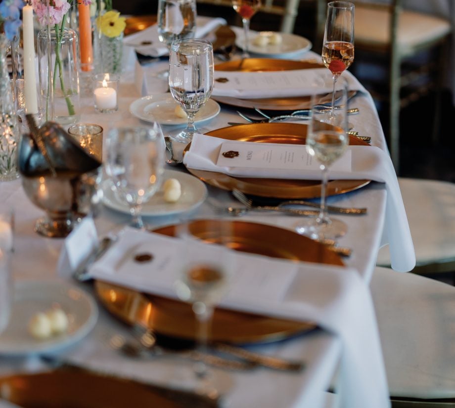 Elegant formal dinner table with gold charger plates, candles, and pink floral centerpieces on white linens.