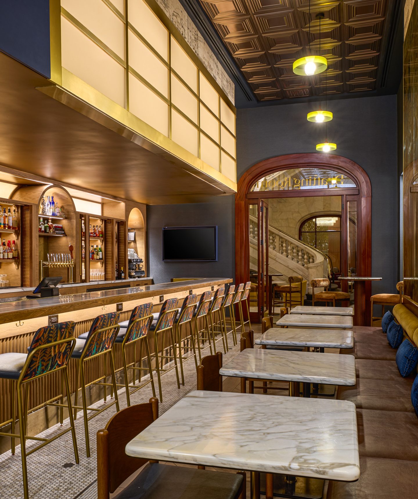 Modern bar interior with marble countertops, wooden stools, and warm pendant lights along a long bar.