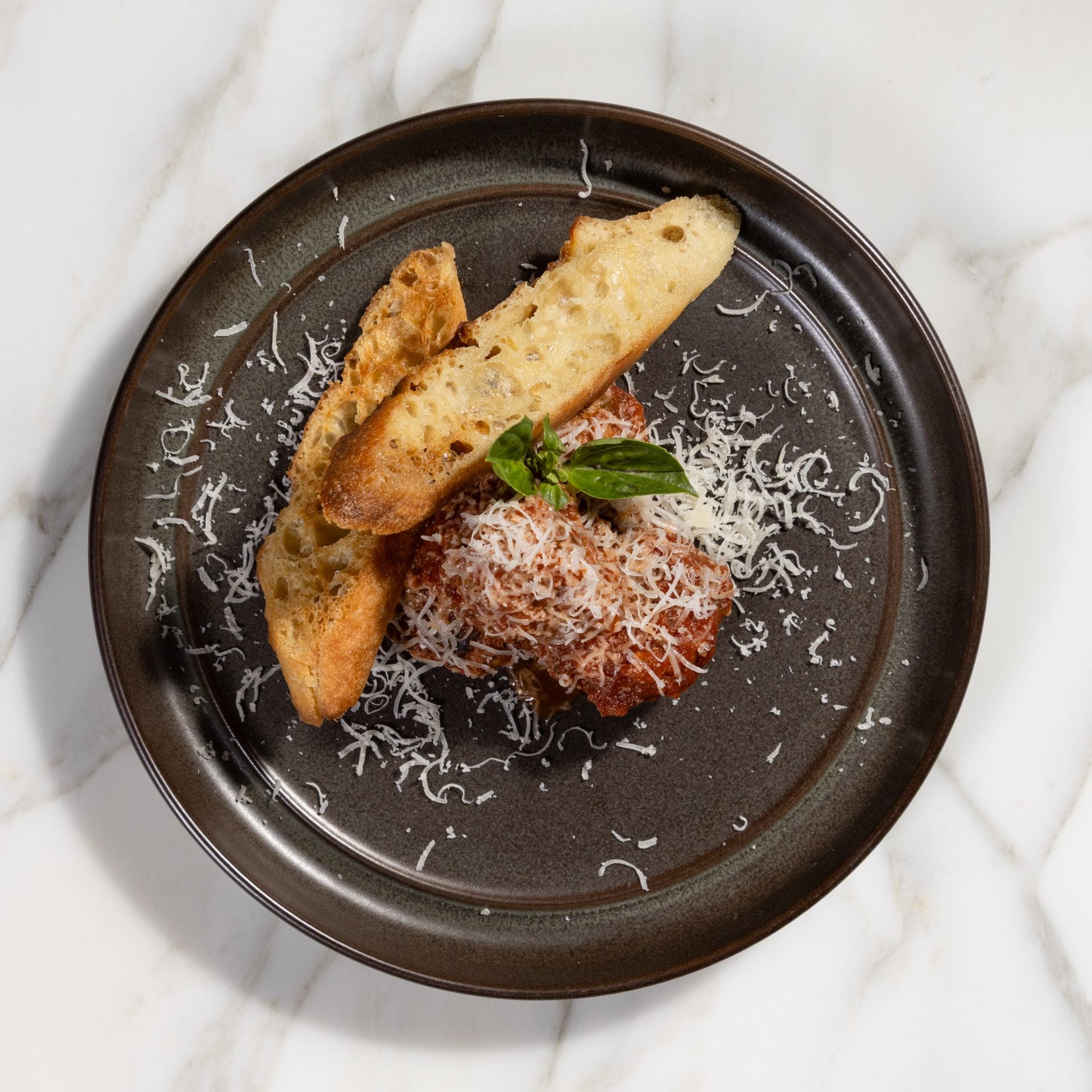 Plate with toasted bread slices topped with tomato sauce, grated cheese, and a basil garnish on a dark plate.