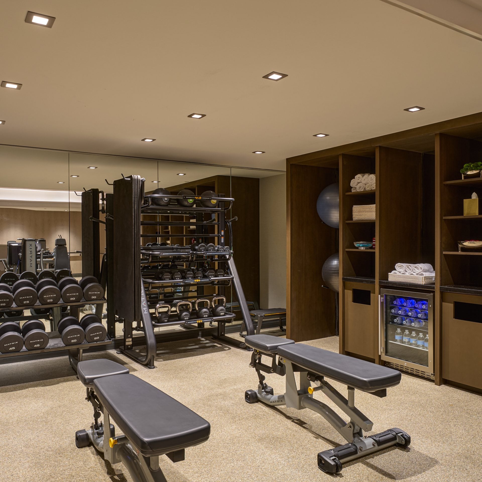 Fitness room with a dumbbell rack, adjustable benches, and a wall of wooden shelves storing towels and equipment.